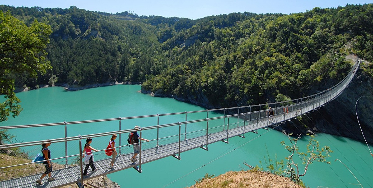 Personnes marchant sur une passerelle pont de singe pour traverser le lac entouré de verdure en été