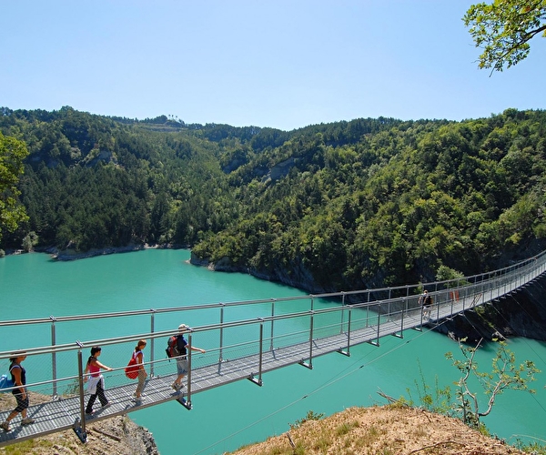 Personnes marchant sur une passerelle pont de singe pour traverser le lac entouré de verdure en été