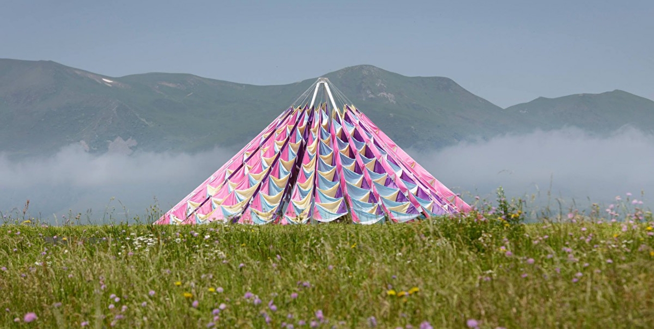Chapiteau artistique aux couleurs vives dans un pré fleuri face aux montagnes
