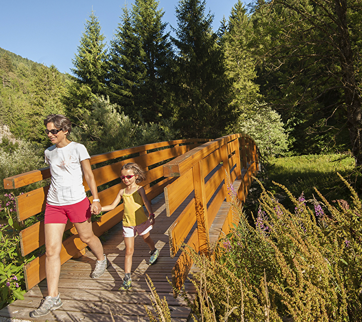 Maman et sa fille en randonnée sur un pont en bois en montagne