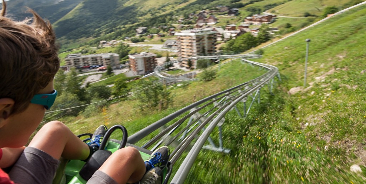 Garçon effectuant une descente en luge d'été sur un rail en pleine nature et proche des montagnes environnantes