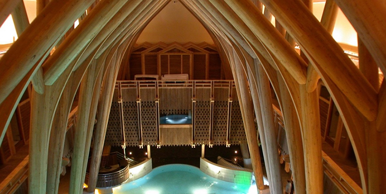 Vue sur la piscine intérieure d'un spa et sur les arches en bois du plafond
