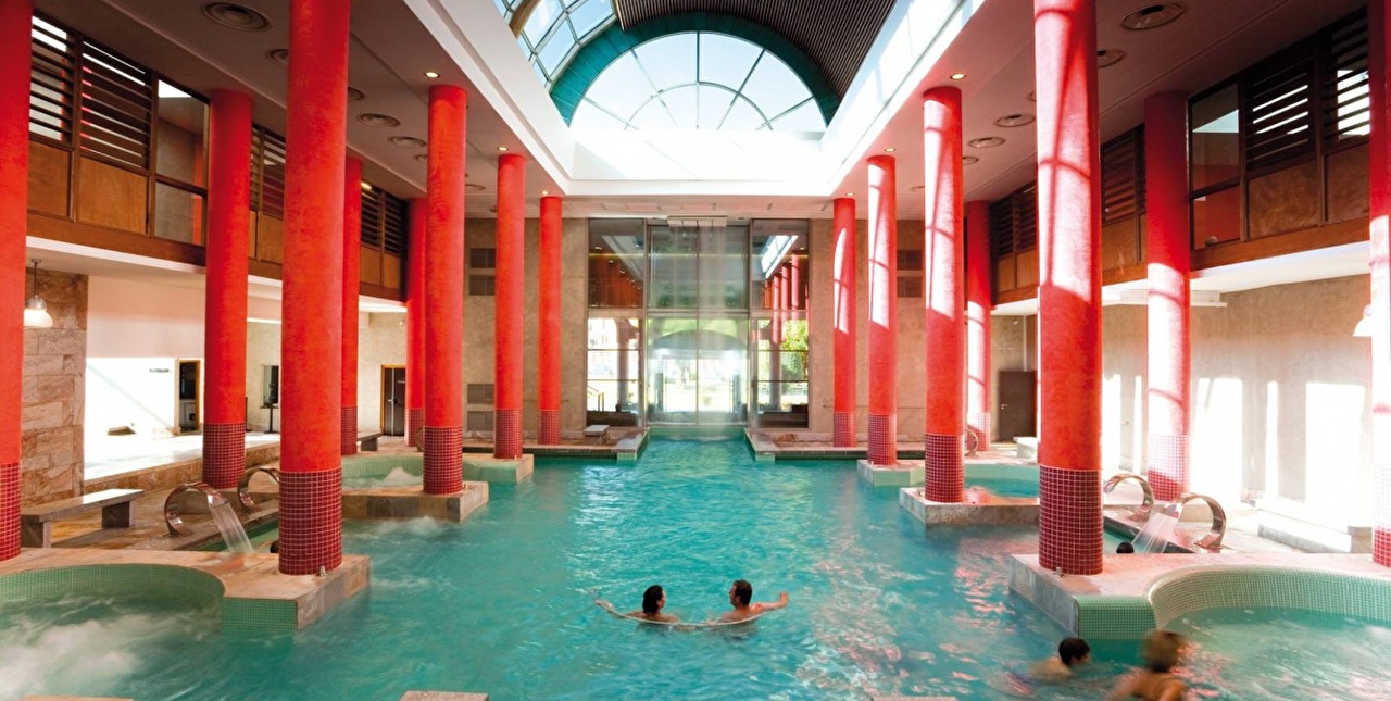 Vue intérieure d'une piscine entourée de colonnes rouges sous une verrière illuminée par le soleil
