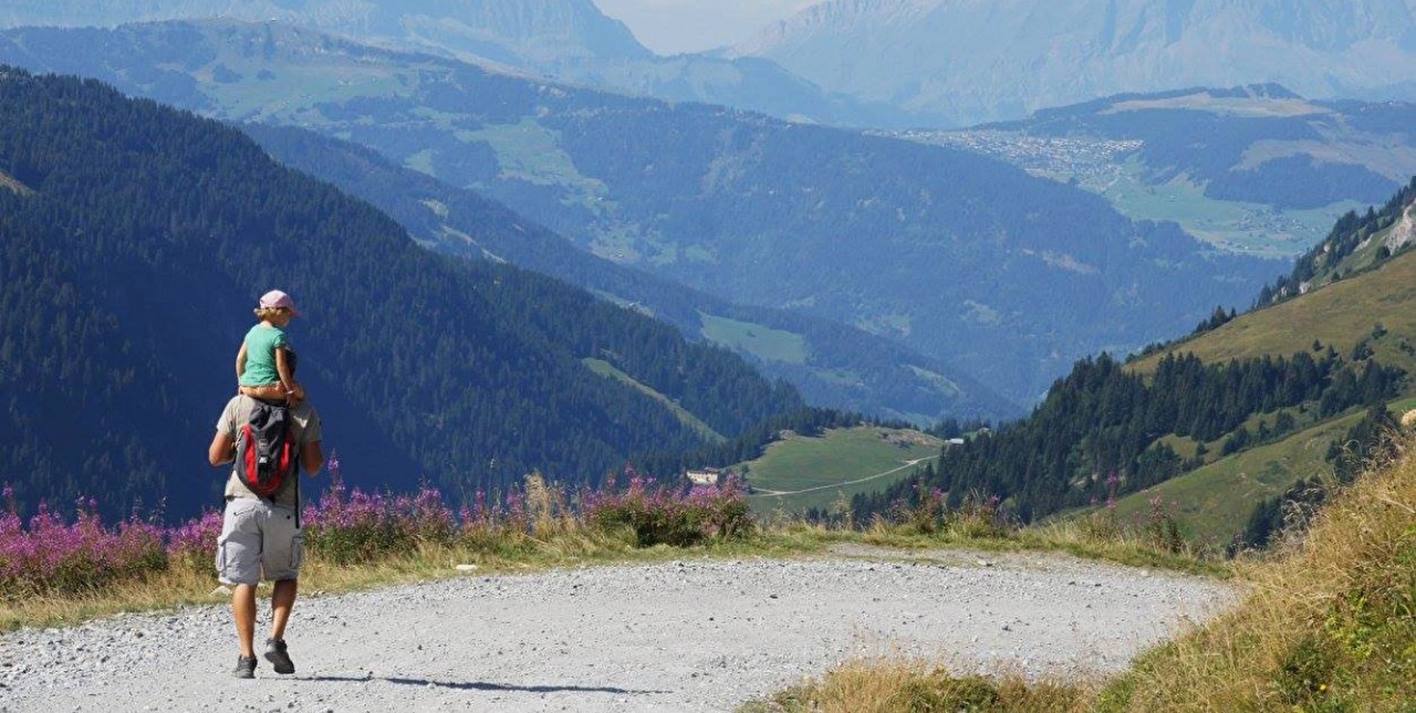 Homme portant un enfant sur ses épaules et se baladant sur un chemin de montagne sous le soleil