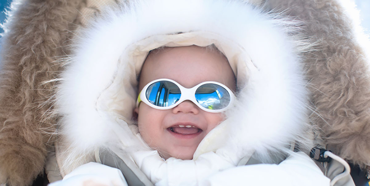 Bébé portant des lunettes de soleil emmitouflé dans une grosse combinaison avec capuche bien chaude