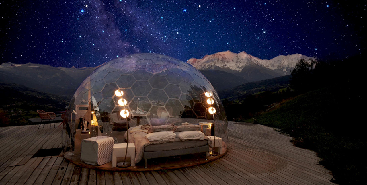 Hébergement bulle et son espace intérieur avec lit et mobilier divers sous les étoiles en montagne la nuit