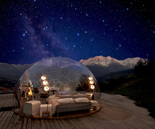Hébergement bulle et son espace intérieur avec lit et mobilier divers sous les étoiles en montagne la nuit