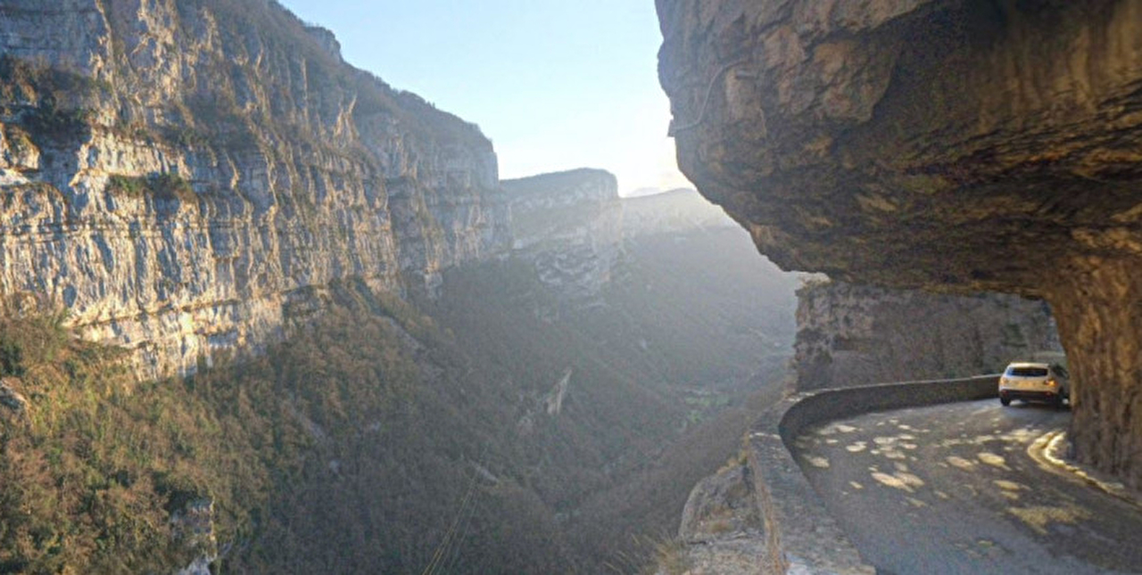 Voiture empruntant un virage sur une route de montagne sous la paroi rocheuse
