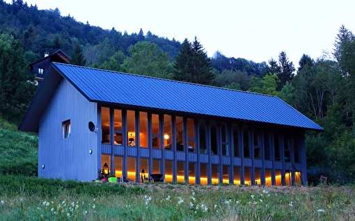 Vue sur un grand chalet aux multiples fenêtres au sein d'un environnement rempli d'arbres et de sapins