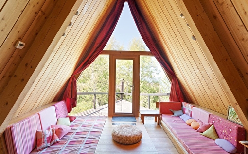 Vue intérieure d'un chalet de montagne avec deux banquettes canapés donnant sur l'extérieur et les arbres