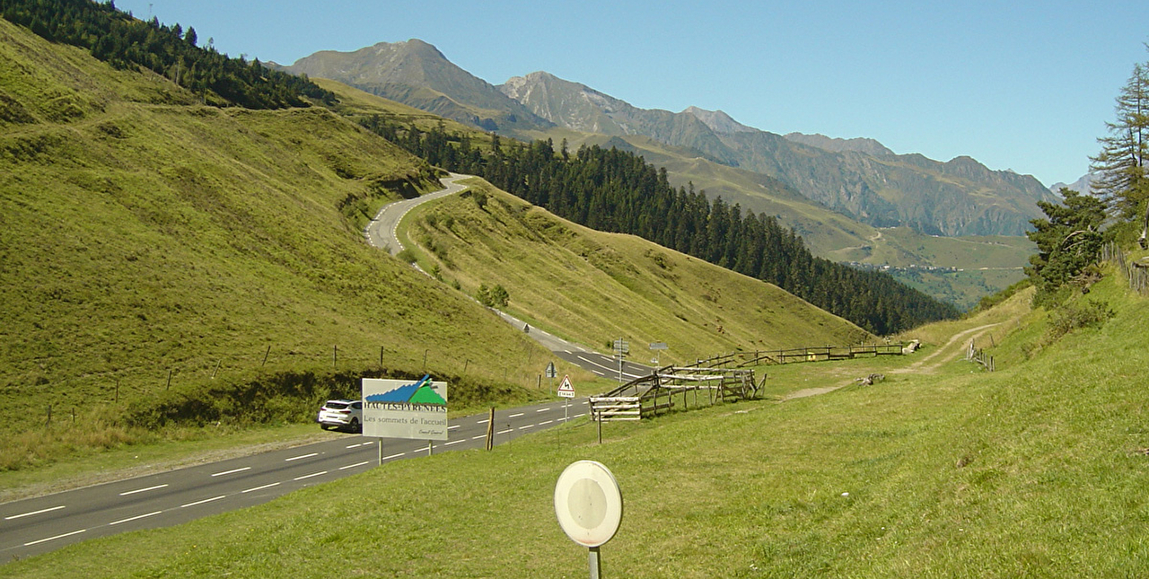 Route traversant un paysage de montagne où forêt de sapins et pâturages longent les abords