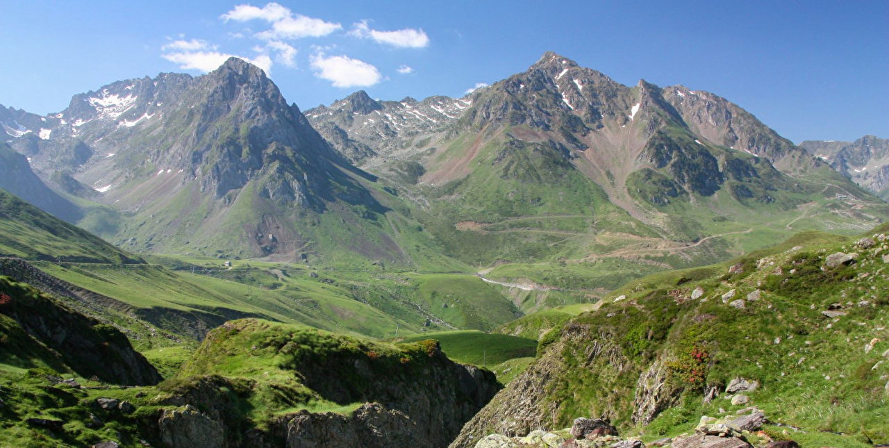 Pics et montagnes rocheuses entourés de verdure sous un ciel avec quelques nuages