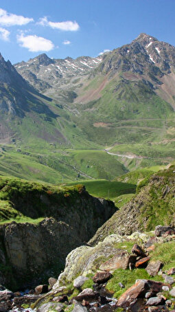 Pics et montagnes rocheuses entourés de verdure sous un ciel avec quelques nuages