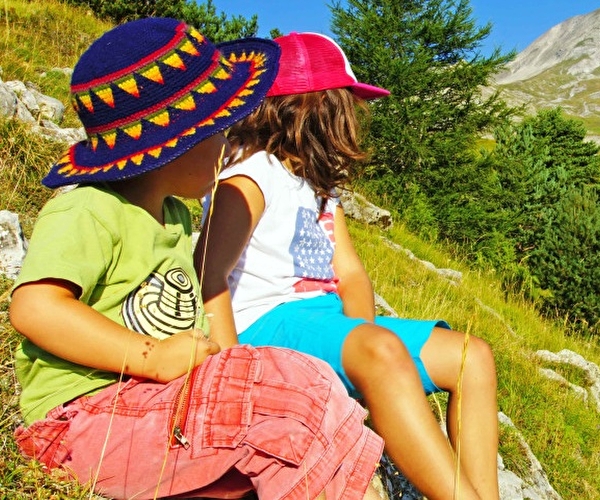 Deux enfants sont assis sur des rochers lors d'une randonnée et admirent les montagnes en été