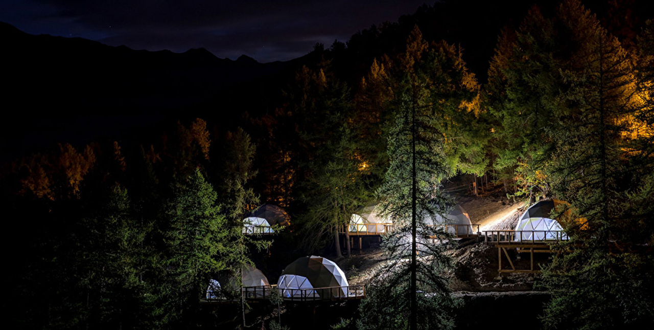 Vue sur des hébergements dômes en plateforme situés en montagne la nuit
