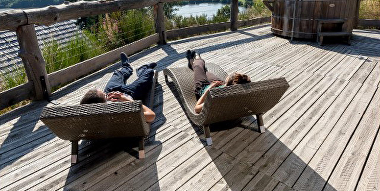 2 personnes allongées dans des chaise-longues en bois se reposent en plein air face à la montagne