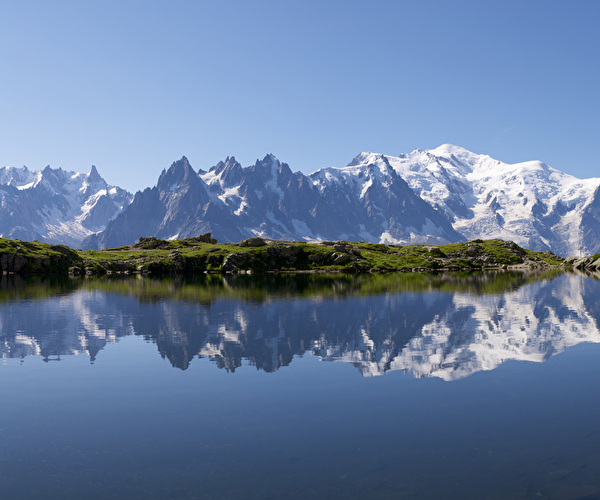 Vue sur un lac de montagne entouré de verdure et vue sur les montagnes environnantes parsemées de neige