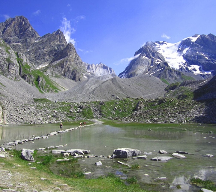 Personnes traversant le lac sur une rangée de pierres plates avec panorama sur les montagnes en été