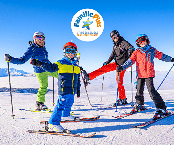 Famille avec deux parents et deux enfants sur une piste de ski avec logo du label Famille Plus