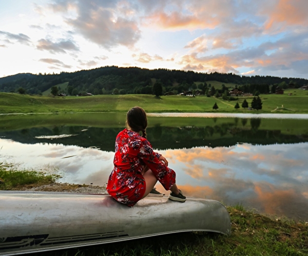 Jeune femme assise sur un canoë face à la montagne observant un lac et la vue sur la montagne