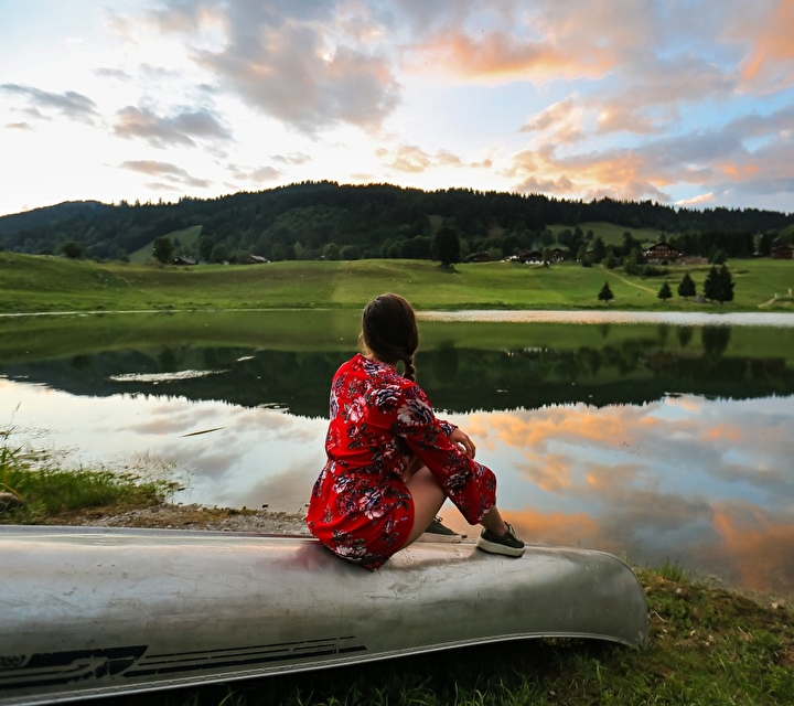 Jeune femme assise sur un canoë face à la montagne observant un lac et la vue sur la montagne