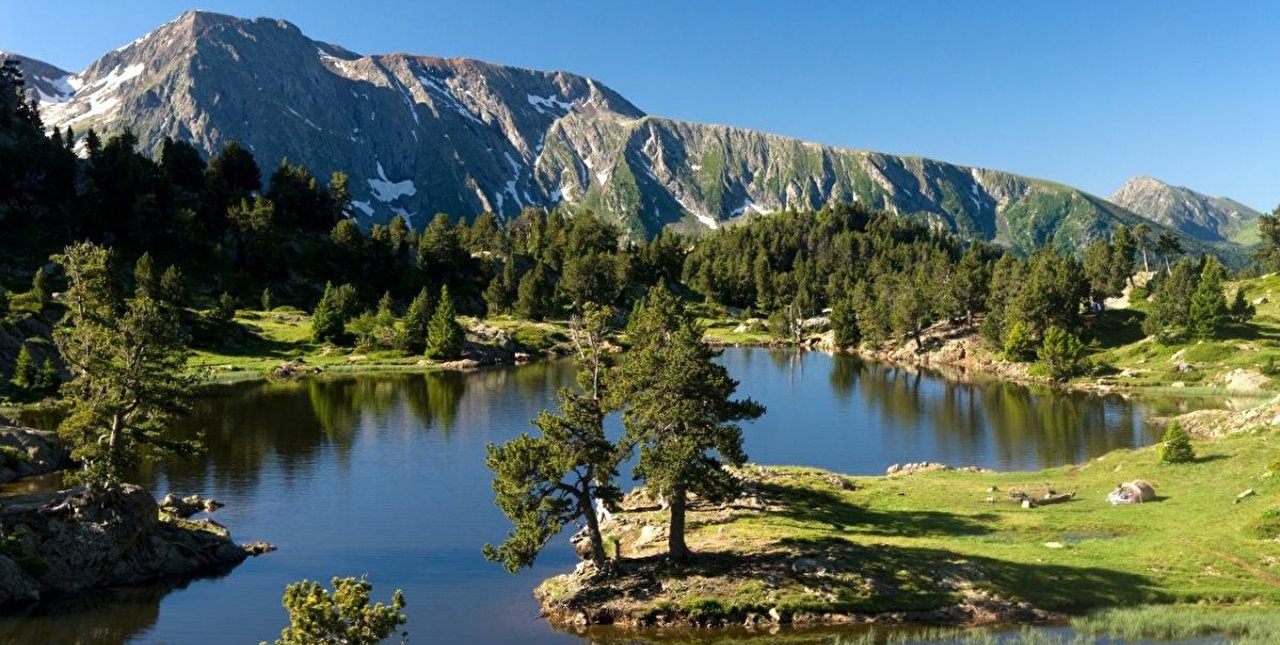 Montagnes et lac entourés de verdure et d'arbres sous un ciel limpide