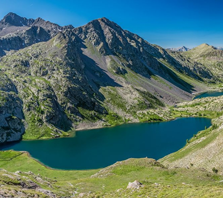 Vue sur un lac couleur turquoise entouré de verdure et de montagnes sous un ciel limpide
