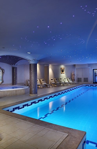 Vue sur la piscine intérieure illuminée d'un spa et son espace détente