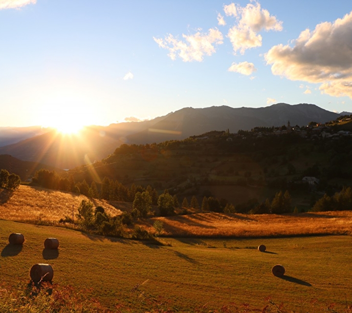 Coucher de soleil et vue sur une prairie en montagnes à travers les champs et ballots de paille