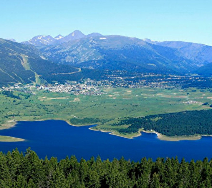 Vue sur le village et un lac entourés de verdure, de sapins et des montagnes