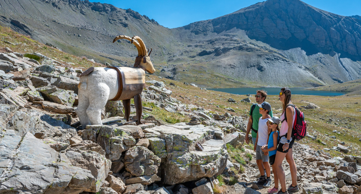 Famille en randonnée observant des sculptures en bois avec vue sur les montagnes