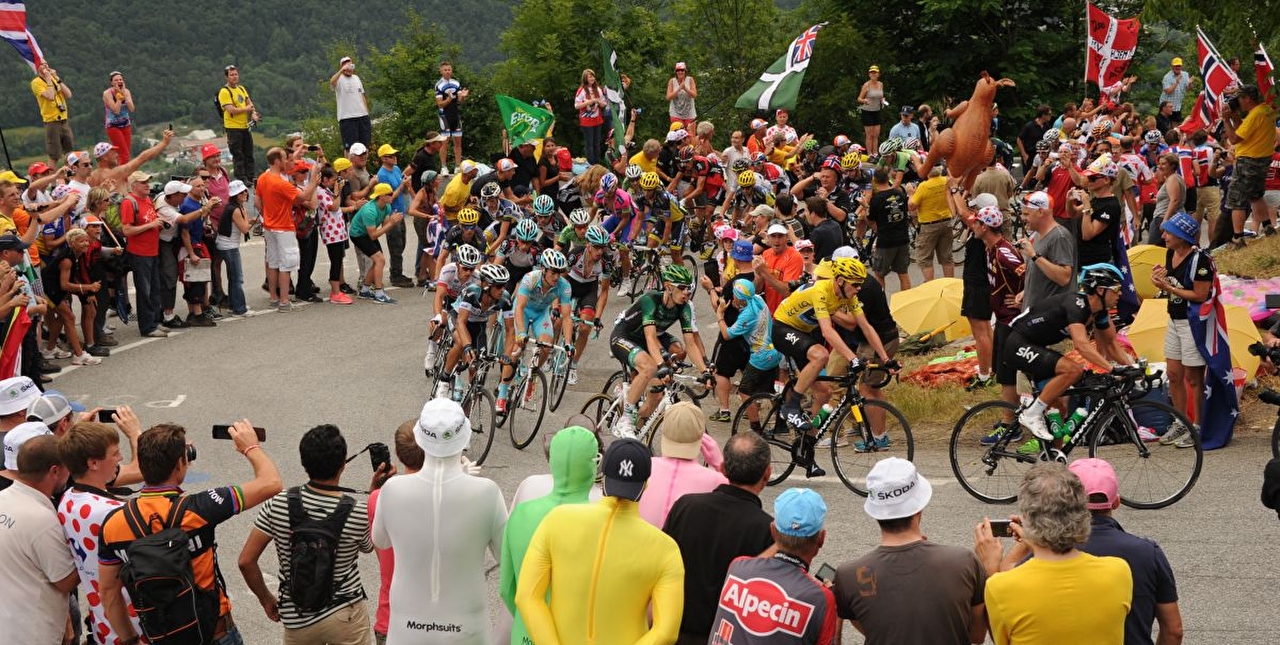 Peloton de cyclistes à vélo grimpant le col devant une foule massée aux abords en montagne