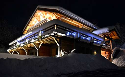 Vue sur un chalet de montagne éclairé en extérieur et sous la neige