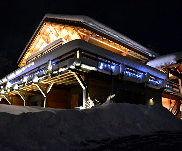 Vue sur un chalet de montagne éclairé en extérieur et sous la neige