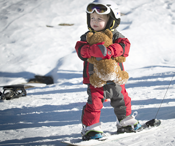 Jeune enfant sur un snowboard avec une peluche dans ses bras