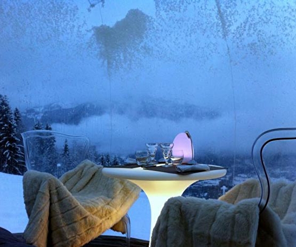 Table dressée sous une bulle pour 2 personnes avec fauteuils et plaids en fourrure à la montagne
