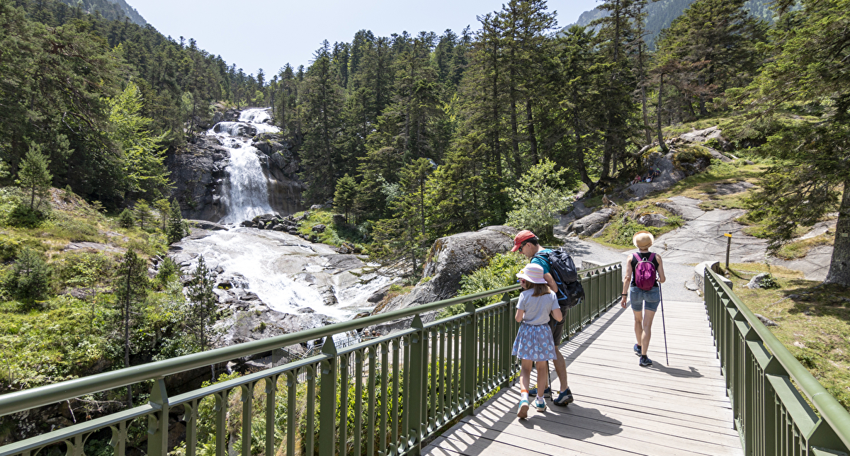 Famille en randonnée sur un pont en bois avec vue sur les montagnes et une cascade