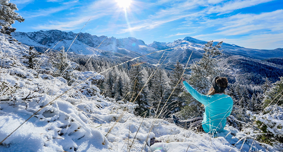 Jeune femme assise dans la neige au soleil avec vue sur les sommets