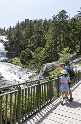 Une famille marche sur un pont, admirant une cascade lors d'une randonnée dans les magnifiques Pyrénées.
