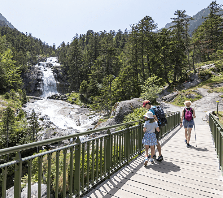 Une famille marche sur un pont, admirant une cascade lors d'une randonnée dans les magnifiques Pyrénées.