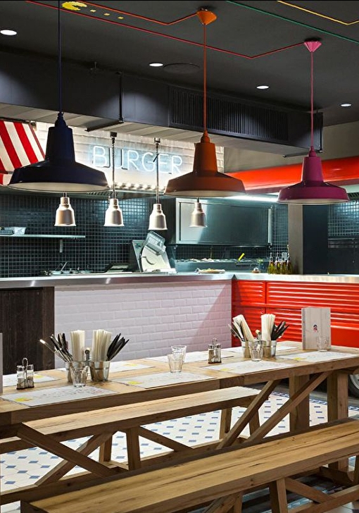 Intérieur d'une cuisine aménagée et colorée en mode food-truck avec une table en bois dressée et plusieurs bancs pour accueillir les vacanciers
