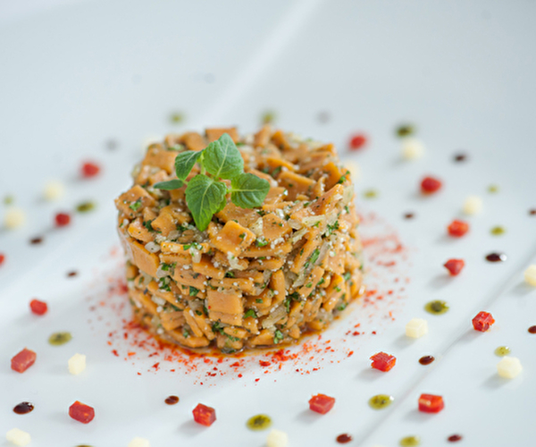 Présentation d'une salade de crozets à la tomate et au piment sur une assiette jolie décorée de pointes de couleurs vertes et oranges