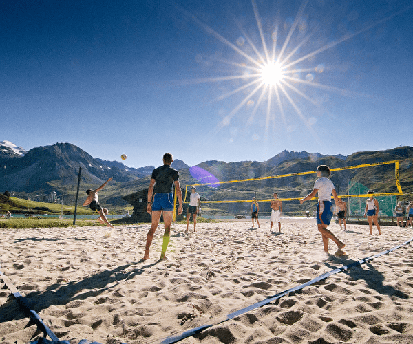 Sportifs effectuant un beach-volley sur le sable et sous le soleil proche d'un lac entouré de montagnes