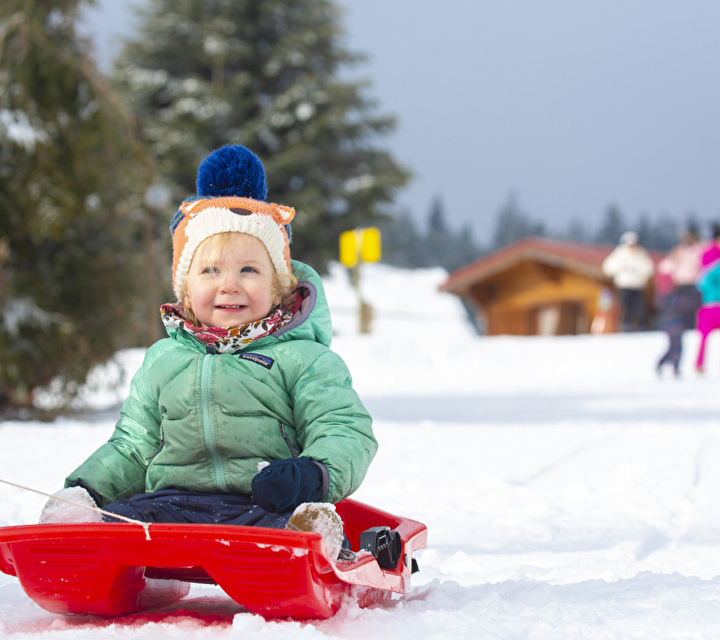 Jeune enfant assis dans une luge roule sur une piste avec sapins enneigés