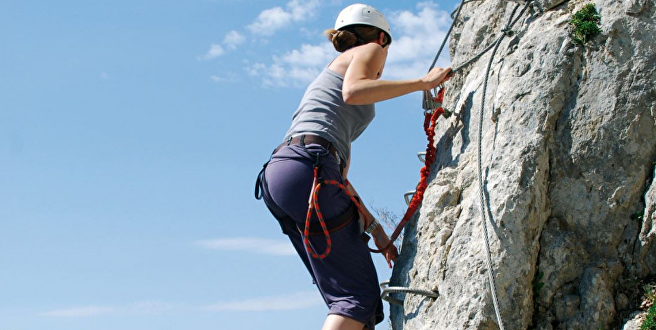 Jeune femme pratiquant l'activité via ferrata en montagne l'été