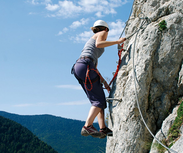 Jeune femme pratiquant l'activité via ferrata en montagne l'été