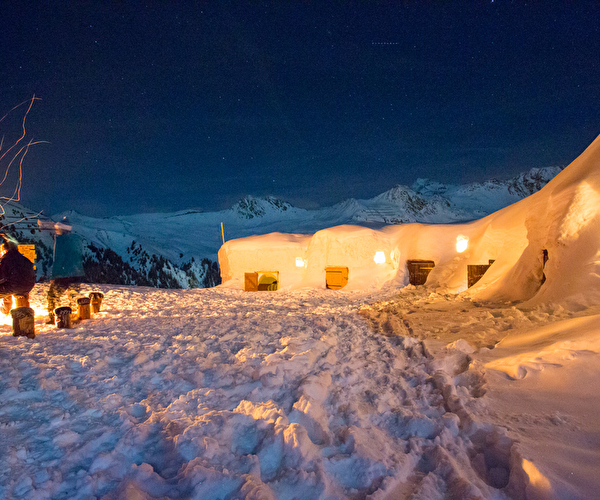 Village igloo illuminé en pleine montagne où plusieurs personnes sont réunies autour d'un feu
