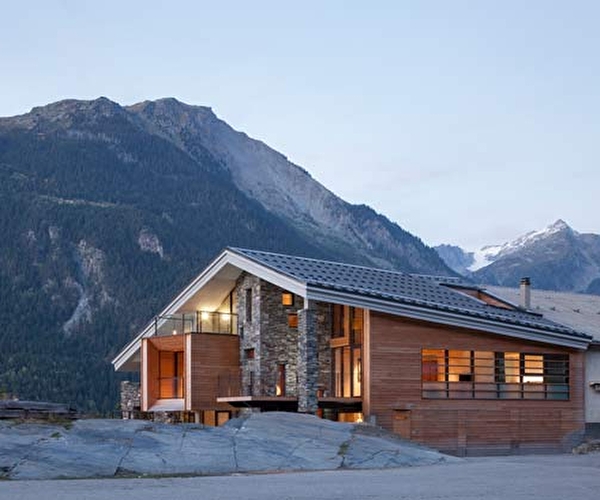 Vue extérieure sur un chalet de bois et pierres éclairé face à la montagne