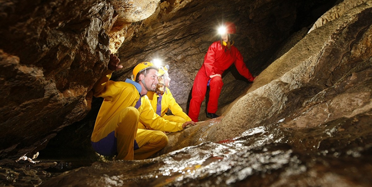 Personnes équipés de tenues imperméables et lampes frontales s'exerçant à une immersion sous terre en spéléologie