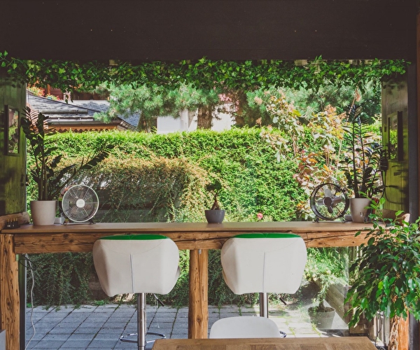 Espace bureau décoré et composé d'une table haute et de fauteuils face à la végétation d'un jardin